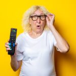 Zdziwiona blondynka staruszka w okularach, trzymając pilota