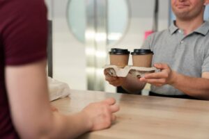 Biały mężczyzna z zespołem Down'a daje klientowi kawę na wynos