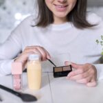 Młoda atrakcyjna kobieta robi makijaż, kobieta siedzi w domu przy stole w kuchni z pędzlem lustro produktów kosmetycznych, pokazuje makijaż cień do brwi. Uroda, pielęgnacja skóry, moda, koncepcja makijażu
