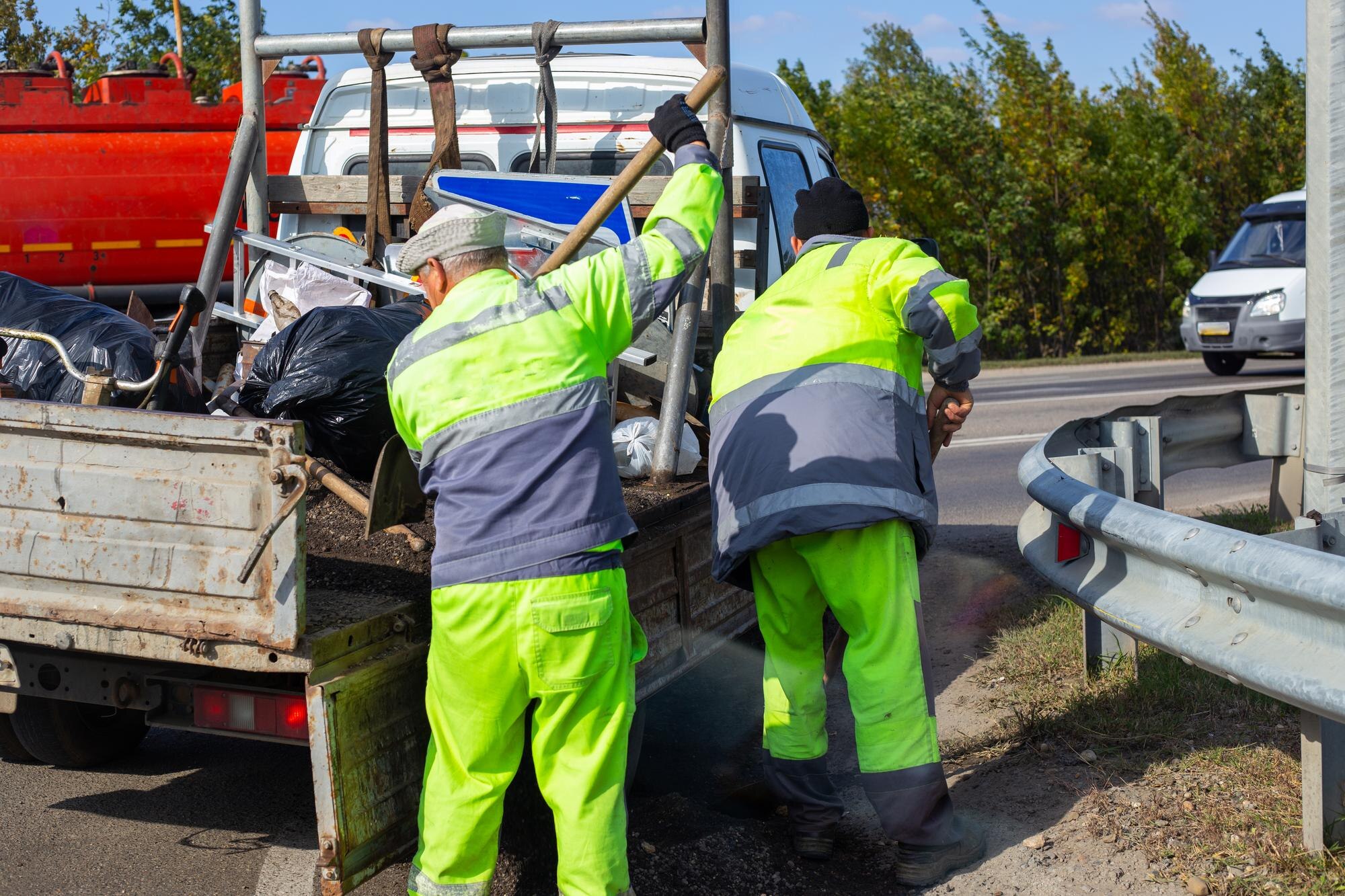 Robotnicy przydrożni w kombinezonach z łopatami sprzątają drogę i wsypują gruz do dziur