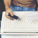 Młody człowiek używa kredytową kartę dla płacić rachunki na laptopie