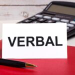 Na biurku bordowy notes kalkulator długopis i biała kartka z napisem VERBAL Business concept