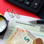 Niemiecki formularz zwrotu podatku dochodowego z długopisem i europejskimi banknotami euro leżą na fladze z bliska Podatnicy w Niemczech używający waluty euro do płacenia podatków