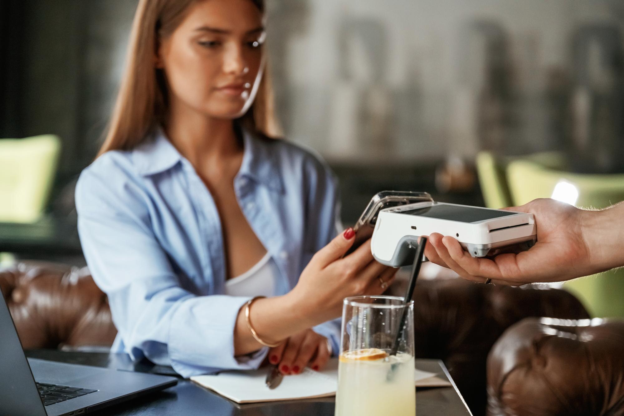 Korzystając ze smartfona Kobieta płaci za usługę w restauracji