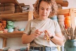 Kobieta robi naturalne bezpieczne akcesoria z drewna na biurku w stylu eko Koraliki sznurkowe Gryzak z dekoracją z grzechotką