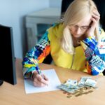 Zamyślona kobieta w średnim wieku licząca pieniądze w euro i robiąca notatki przy biurku w domowym biurze