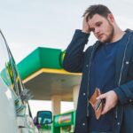 Mężczyzna ze smutnym widokiem i pustym portfelem na stacji benzynowej dolary pieniądze w zbiorniku samochodowym