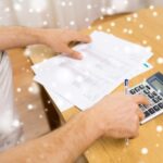 biznes, oszczędności, finanse i koncepcja ludzi - zbliżenie rąk człowieka z papierami i kalkulatorem w domu nad efektem śniegu