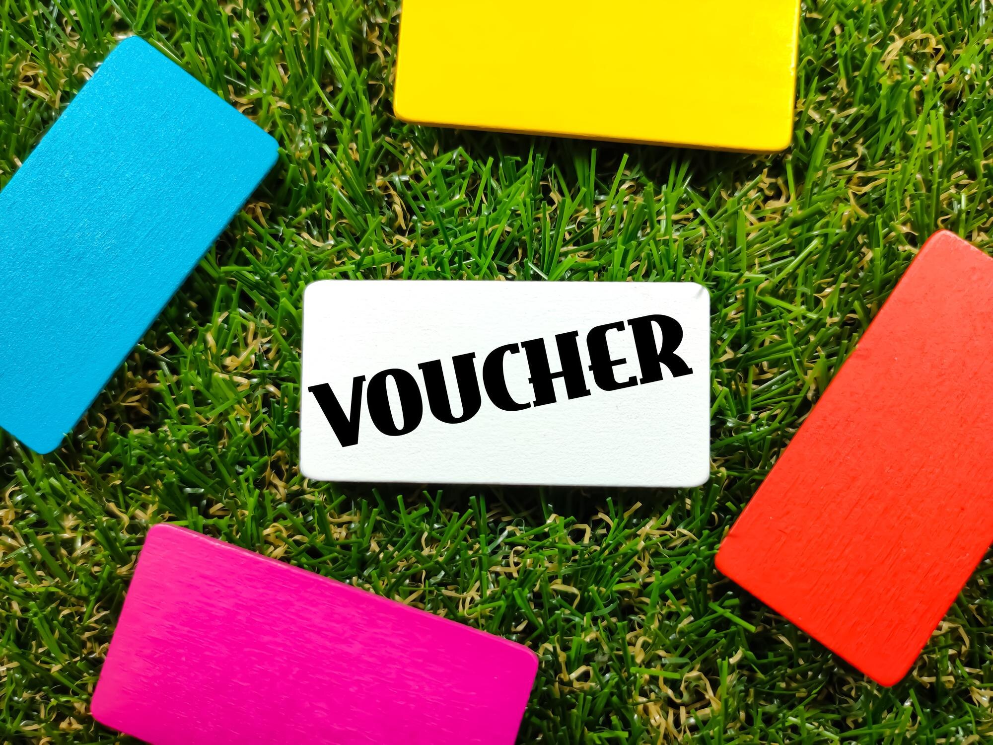 Kolorowa drewniana deska z tekstem VOUCHER na trawiastym tle
