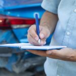 Agent ubezpieczeniowy z notatnikiem w pobliżu zniszczonego samochodu