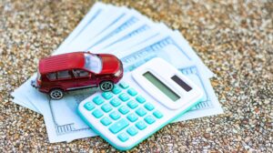 Model samochodu i kalkulator na banknotach euro na niewyraźnym tle Planowanie oszczędzania na zakup samochodu