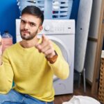 Latynos robi pranie trzymając skarbonkę wskazując palcem na kamerę i na ciebie, pewny siebie gest wyglądający poważnie