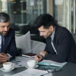 two men sitting at a table working on a laptop